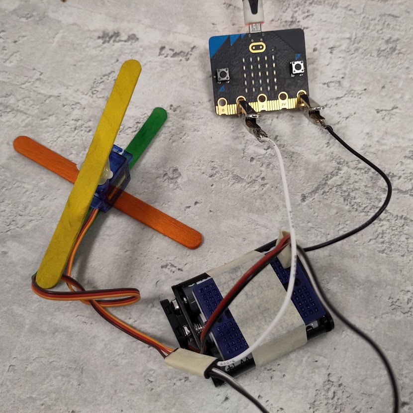 photograph of a BBC micro:bit. A crocodile clip with a white wire is attached to the gold pin labelled 1, second from the left. A crocodile clip with a black wire is attached to gold pin labelled GND, furthest right.